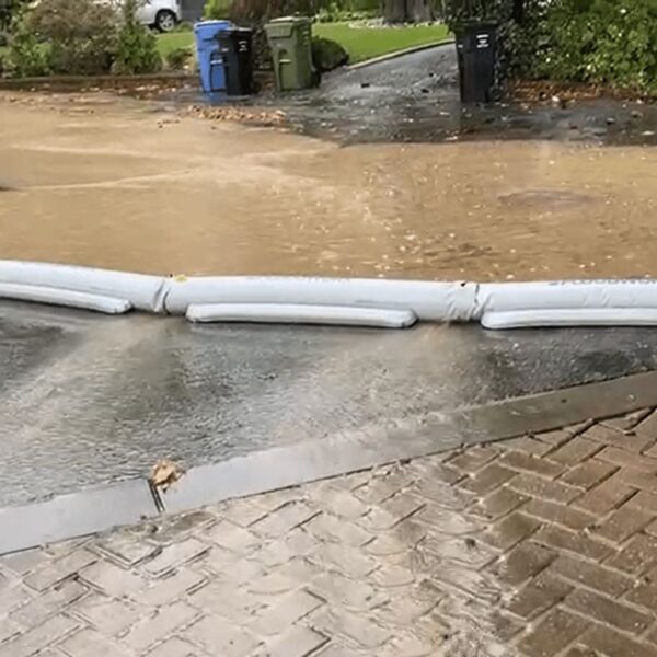 Mehrere verbundene Floodworx Wasserschutzschläuche dämmen Hochwasser ein und leiten es zum Kanal.