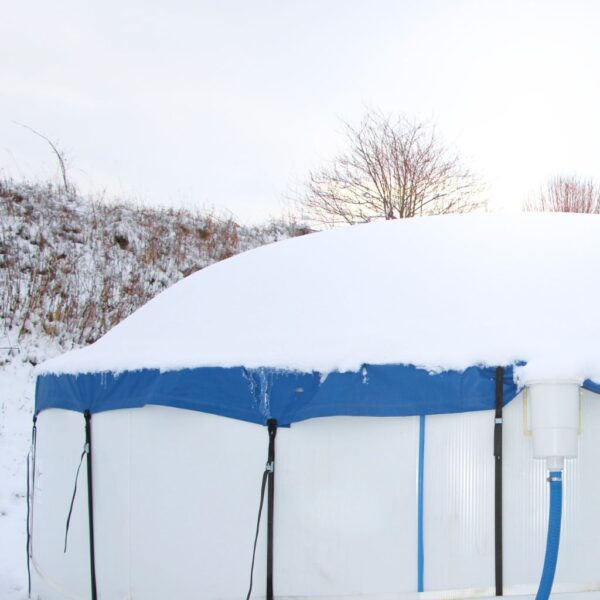 Ein mit Schnee bedeckter, runder Pool der mit einem Poolkissen, einer Abdeckplane und robusten Zurrgurten winterfest gemacht ist.